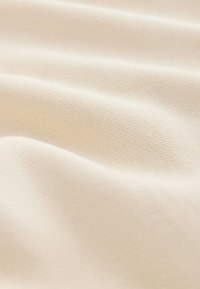Gros plan sur un tissu doux de couleur crème avec une texture fine et des plis délicats.