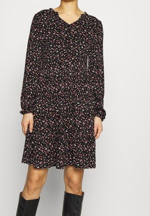 Femme portant une robe noire à manches longues avec un petit imprimé floral rose et blanc, associée à des bottes noires hautes jusqu’au genou.