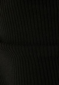 Tissu côtelé noir avec des lignes verticales, présentant une surface texturée. Le matériau semble doux et extensible, conçu pour un port confortable.