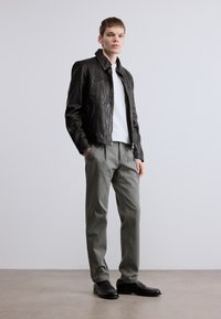 Μαύρο δερμάτινο μπουφάν με γιακά, λευκό μπλουζάκι, ανοιχτό γκρι παντελόνι και μαύρα μοκασίνια· λεία υφή και ραμμένο για τέλεια εφαρμογή.