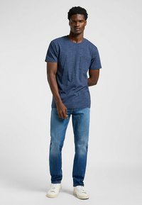 Mörkblå T-shirt med kort ärm, rund halsringning och bröstficka, i kombination med ljusblå jeans och vita sneakers.