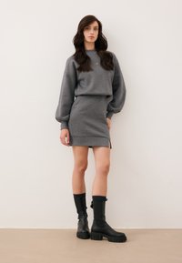 Szary sweatshirt z opadającymi ramionami, dopasowana ołówkowa spódnica i czarne buciki do kolan z teksturowaną podeszwą. Prosty design, bez wzorów.