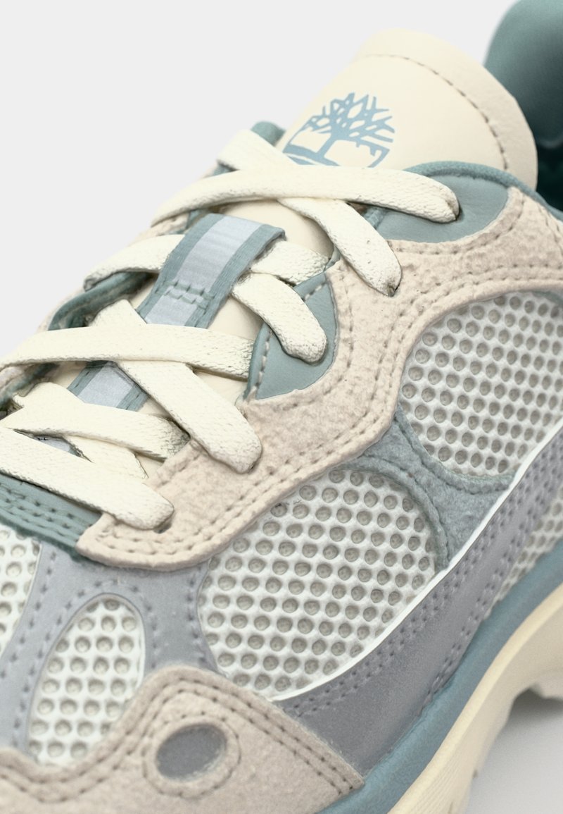 Sneaker grigio chiaro e blu con pannelli in camoscio e mesh, e suola in gomma. I dettagli includono un logo cucito e lacci piatti.