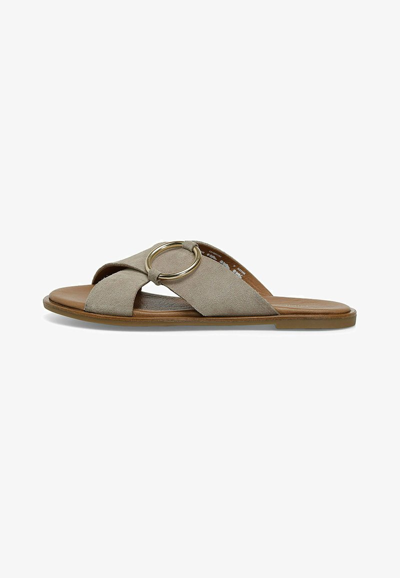 Beige ruskinds slip-on sandal med et tværbåndsdesign, en guldrund detalje og en flad brun sål. Glat tekstur.
