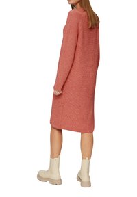 Strickkleid in Koralle mit gerader Silhouette, geripptem Textur, langen Ärmeln und seitlichen Schlitzen, kombiniert mit cremefarbenen Ankle Boots.