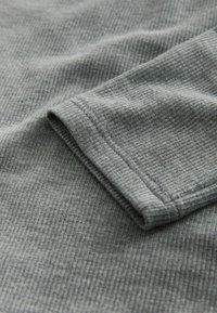 Grau gerippter Stoff mit glatter Textur, der einen gefalteten Ärmelrand und subtile Nähdetails zeigt.