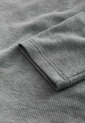 Hallikas sooniline kangas, millel on sile tekstuur, näidates volditud varruka äärt ja peeneid õmblusdetailsid.