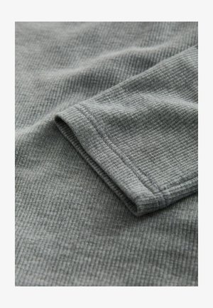 Hallikas sooniline kangas, millel on sile tekstuur, näidates volditud varruka äärt ja peeneid õmblusdetailsid.