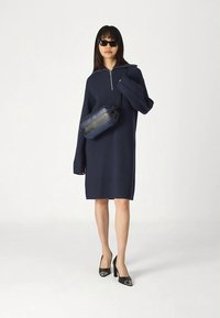 Laivastonsininen ribbineulottu mekko, jossa on pitkät hihat ja vetoketjullinen kaulus. Yhdistetty mustaan ja laivastonsiniseen olkalaukkuun sekä mustiin korkokengiin.