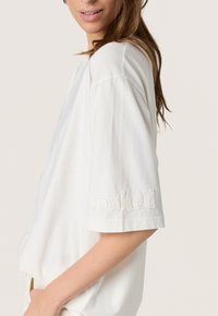 Hvid bomulds t-shirt med løs pasform, korte ærmer og "soaked" broderet i en let hævet tekstur på ærmet.