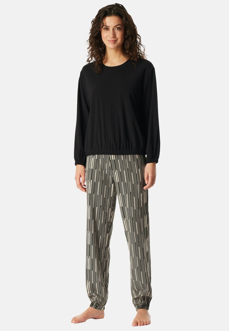 Zwarte lange mouwen top met een elastische onderrand, gecombineerd met een patroon van wijde broek met verticale strepen in zwart en crème.