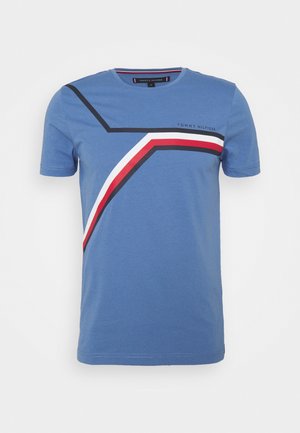 T-shirt bleu à manches courtes avec un design géométrique de rayures noires, blanches et rouges sur la poitrine et le texte "Tommy Hilfiger" en haut à droite.