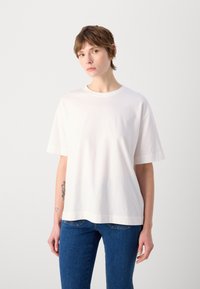 Vit bomullströja med korta ärmar, rund halsringning och avslappnad passform, kombinerad med blå denimjeans. Lätt struktur, inga synliga mönster.