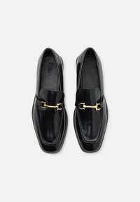 Mocassins en cuir noir au design épuré, à bout carré, avec des détails décoratifs en metal doré sur le devant. Texture lisse et finition brillante.