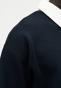 Σκούρα μπλε πλεκτή πουλόβερ με υφή και αντίθετο λευκό γιακά. Διαθέτει κλασικό σχεδιασμό και χαλαρή εφαρμογή.