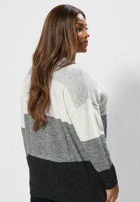 Szary i biały kardigan w paski, wykonany z miękkiej dzianiny. Posiada luźny krój, długie rękawy oraz nieco dłuższy tylny brzeg.