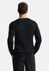 Tengerészkék kábelmintás pulóver texturált mintával, kerek nyakkivágással, bordázott mandzsettákkal és alsó szegéllyel. Az anyag vastagnak és melegnek tűnik.