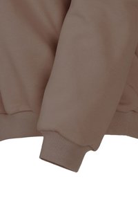 Brązowy rękaw swetra z ribbowanymi mankietami, wykonany z gładkiego, miękkiego materiału. Charakteryzuje się luźnym krojem i minimalisticznym wzornictwem.