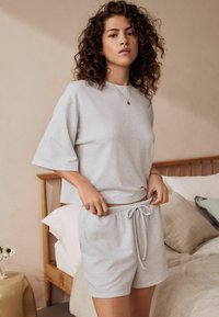Svjetlosiva loungewear set od vaflastog pletenog materijala koji se sastoji od majice kratkih rukava i šorts na vezanje, sa teksturiranim materijalom i opuštenim krojem.