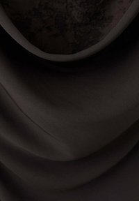 Gros plan d’un tissu noir lisse avec des plis subtils et un bord courbé, mettant en valeur la texture et le drapé.