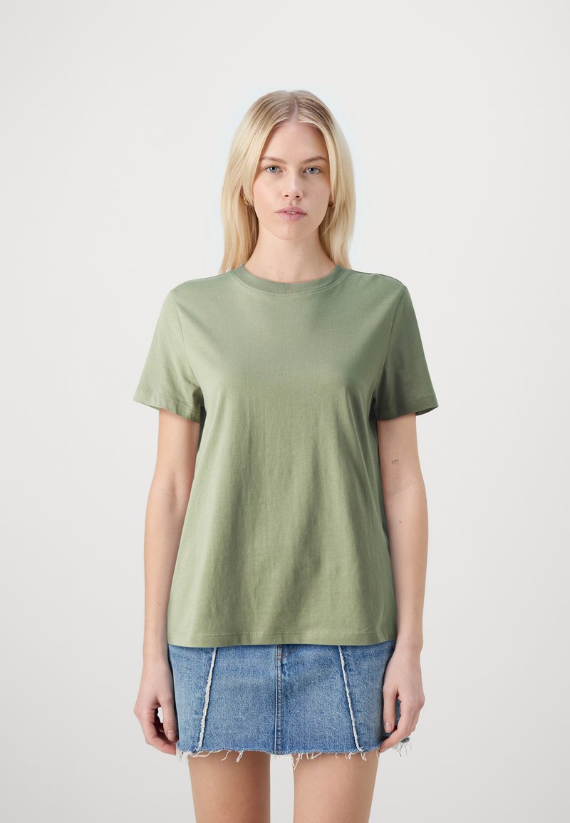 Olijfgroene katoenen t-shirt met korte mouwen, ronde halslijn, ontspannen pasvorm, gecombineerd met een blauwe denim rok met rafelrand en paneeldetails.