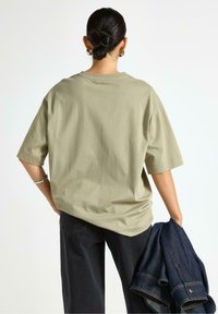 Beige oversize T-shirt med korta ärmar, gjord av mjukt bomullstyg, i kombination med mörka jeans och en denimjacka i handen.