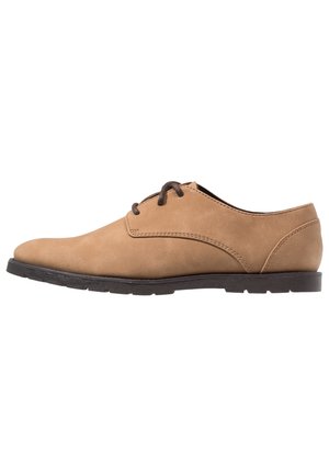 Zapato de vestir de hombre de cuero color tan con cordones y suela negra, visto de perfil sobre un fondo blanco.