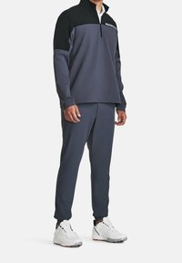 Mørkegrå træningssæt med en halv-lynlås pullover med en sort yoke og matchende tætsiddende bukser, parret med hvide træningssko.