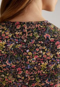 Vestido floral con fondo negro y flores multicolores vibrantes. Incluye una cremallera discreta en la parte posterior para el cierre.