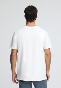 Camiseta de algodón blanca con mangas cortas, escote redondo y un corte holgado. Diseño simple, textura suave, sin patrones ni acentos visibles.