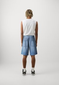 Világoskék farmer rövidnadrág közepes derékkal, hátul két zsebbel és klasszikus öt zsebes kialakítással. Fehér ujjatlan pólóval viselve.