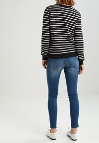 Černobílá pruhovaná mikina s dlouhými rukávy, žebrovanými manžetami a lemem; ve spojení s modrými úzkými džíny a světlými botami.