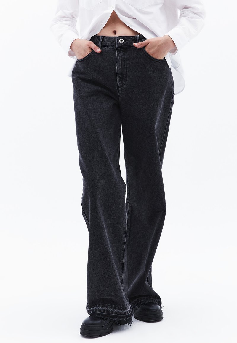 Pantalones de mezclilla anchos negros con cintura alta, que presentan bolsillos delanteros y un dobladillo deshilachado, combinados con calzado negro grueso.