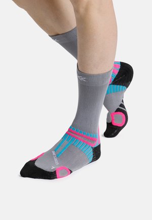 Benen met grijze sportieve sokken tot halverwege de kuit met zwarte, blauwe en roze vulling accenten, getoond op witte achtergrond.