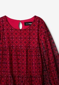 Vestido rojo con un patrón circular en diferentes tonos, escote redondo con un corte de llave y mangas acampanadas con dobladillo rizado.