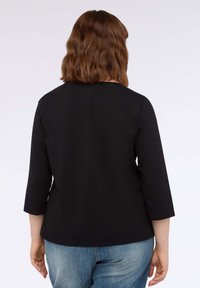 Maglietta nera a maniche lunghe con scollo rotondo e texture morbida, abbinata a jeans blu chiaro, vista da dietro.