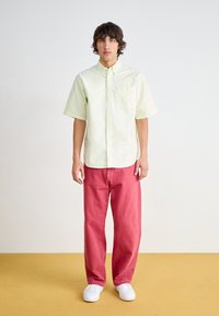 Lysegrønn kortermet skjorte med knapper og frontlomme, kombinert med løspassende rosa jeans og hvite sneakers. Enkelt og uformelt design.