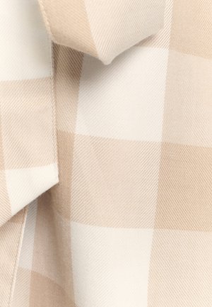 Tissu à carreaux beige et blanc avec un tissage texturé, présentant des grands carrés alternés. Surface lisse avec des lignes diagonales subtiles.