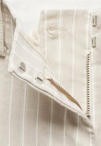Chemise boutonnée beige clair avec des rayures blanches verticales, une fermeture éclair dissimulée et des accents en métal au col et à la patte de boutonnage.