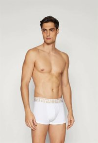 Λευκά boxer briefs με χρυσή ζώνη σχεδίου, εφαρμοστή σχεδίαση, μαλακή υφή και μήκος ποδιών μέτριο. Μοντέλο σε όρθια στάση με ουδέτερη έκφραση.