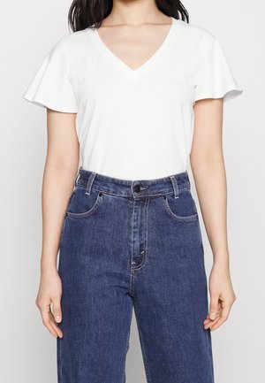 T-shirt blanc à col en V avec manches courtes évasées, associé à un jean denim bleu foncé taille haute avec poches avant et coutures visibles.