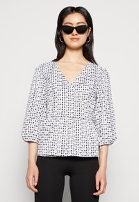 Top de gingham branco e preto com decote em V, mangas bufantes e cintura franzida. O material parece leve e texturizado.
