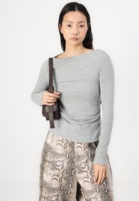 Grijze lange mouwen shirt met een bootnek, gecombineerd met beige broek met slangenpatroon en een kleine bruine schoudertas.