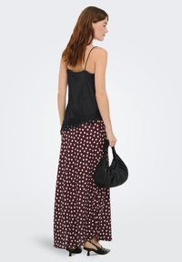 Caraco en satin noir avec bordure en dentelle transparente, associé à une longue jupe bordeaux à pois blancs. Le mannequin tient un sac noir.