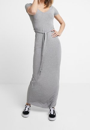 Robe longue en jersey gris avec un col en V et des manches courtes. Caractérisée par une ceinture nouée à la taille et une silhouette fluide. Portée avec des baskets noires.