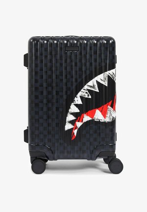 Valigia nera rigida con motivo a scacchiera testurizzato, grafica bocca di squalo in bianco e rosso e quattro ruote girevoli.