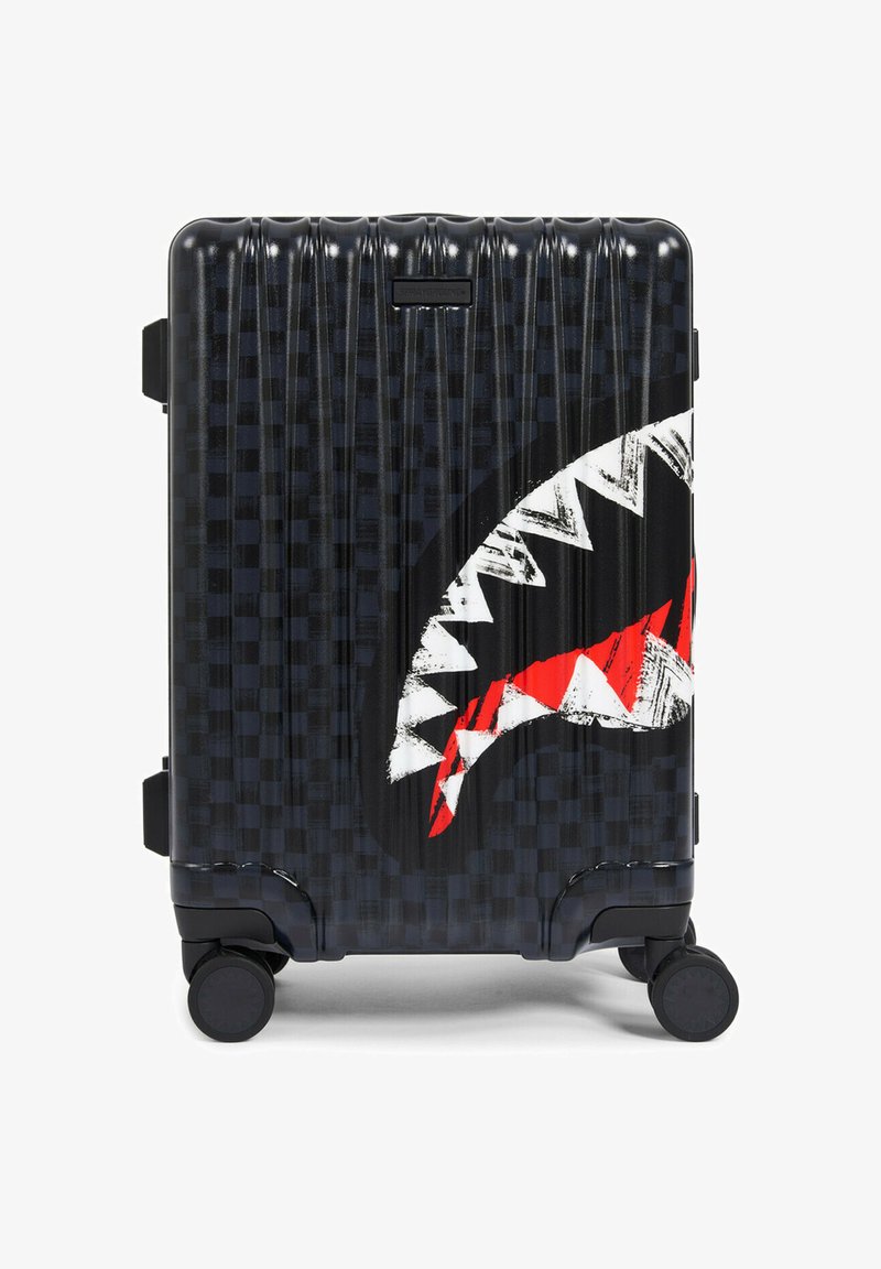 Valigia nera rigida con motivo a scacchiera testurizzato, grafica bocca di squalo in bianco e rosso e quattro ruote girevoli.