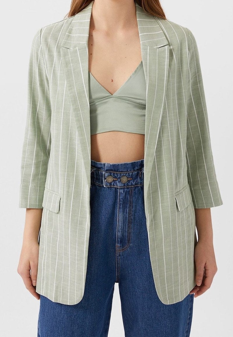 Grüner, gestreifter Blazer mit tailliertem Design, der dreiviertel Ärmel und zwei vordere Taschen aufweist, kombiniert mit einem passenden Oberteil und hochtaillierten Jeans.