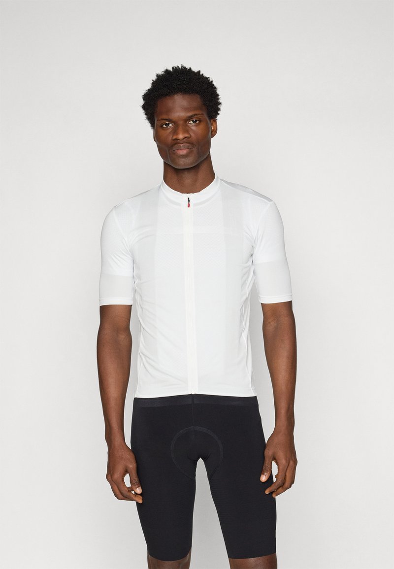 Maillot de cyclisme blanc à manches courtes avec une fermeture éclair à l'avant, au design texturé, et un short de cyclisme noir avec un coussin rembourré.