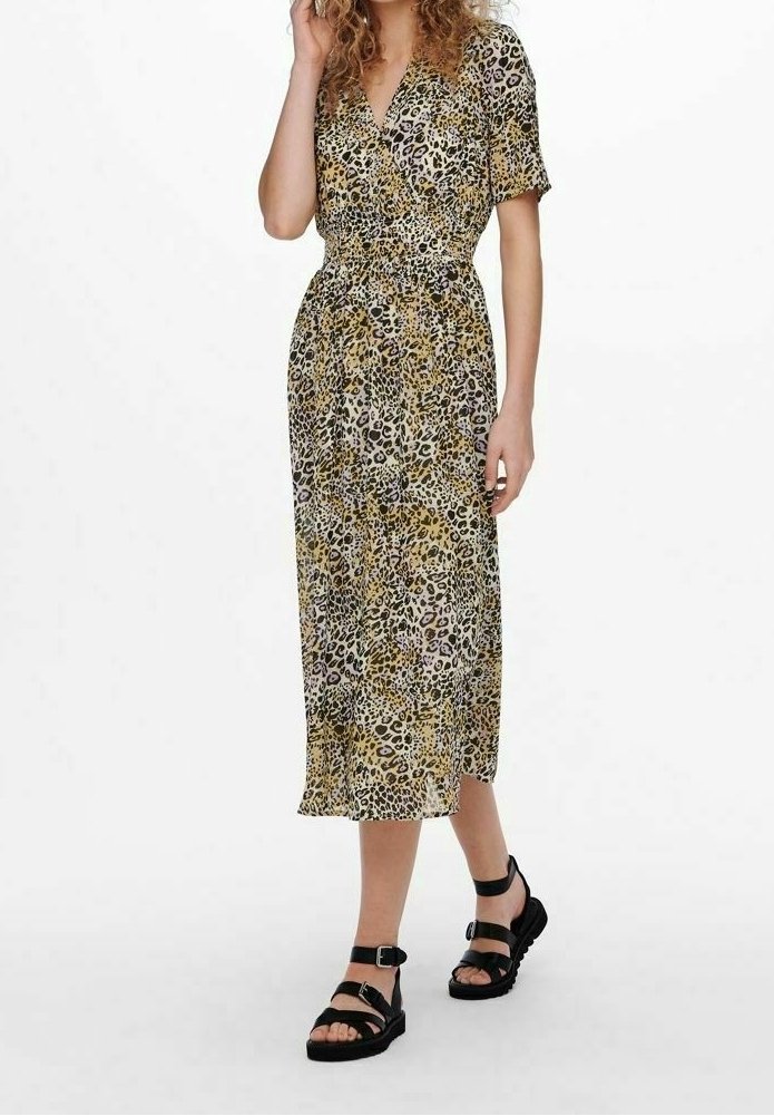 Robe imprimée léopard avec un design enroulé, manches courtes et taille ceintrée. Longueur midi, tissu léger, associée à des sandales noires à lanières.